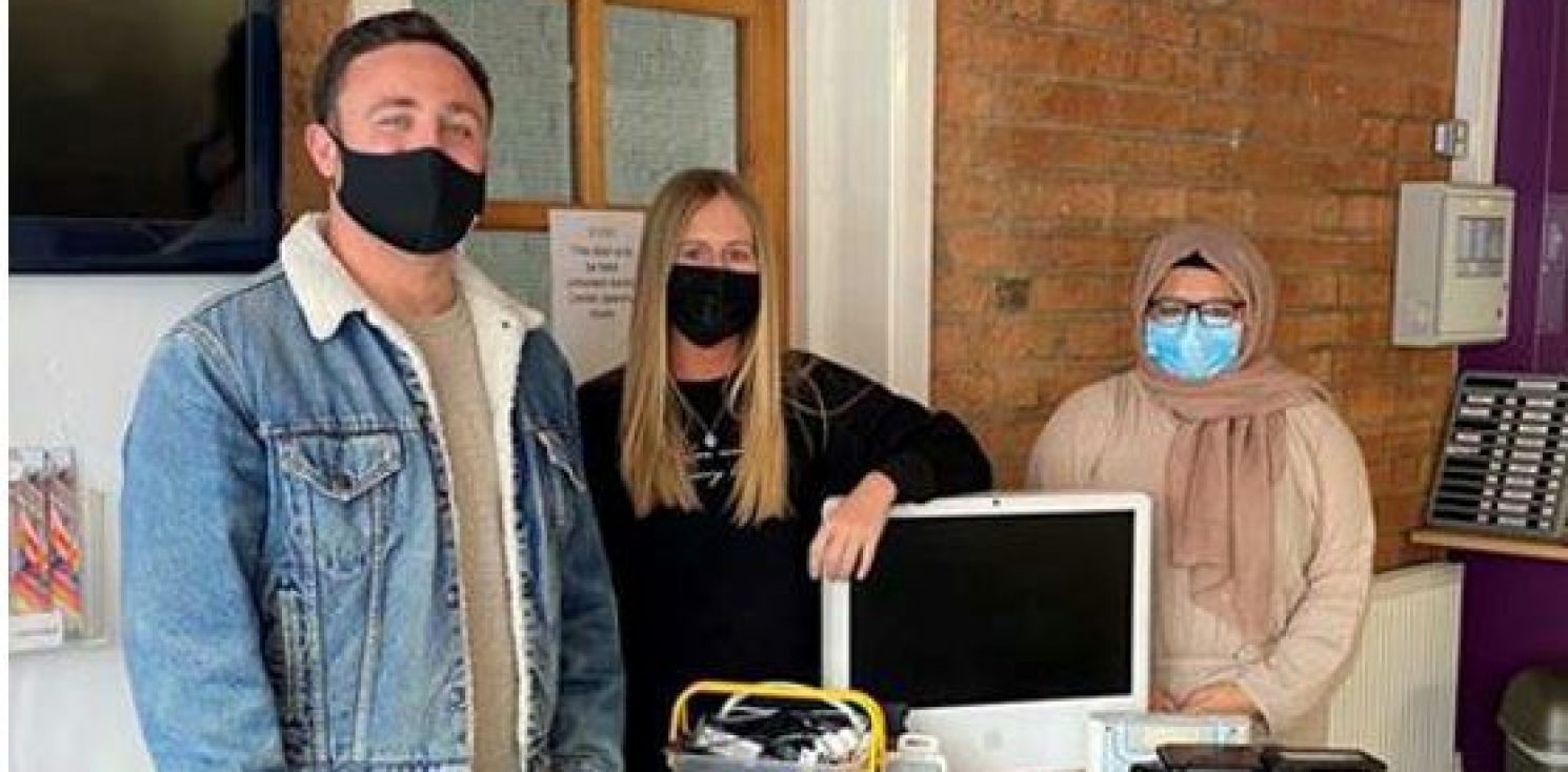 3 people stood around a table filled with used computer electricals that are to be recycled for continued use not thrown away.